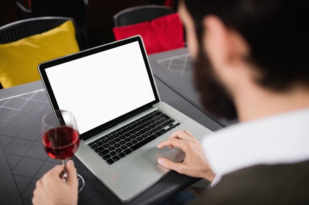 Hombre usando laptop mientras tomando una copa de vino