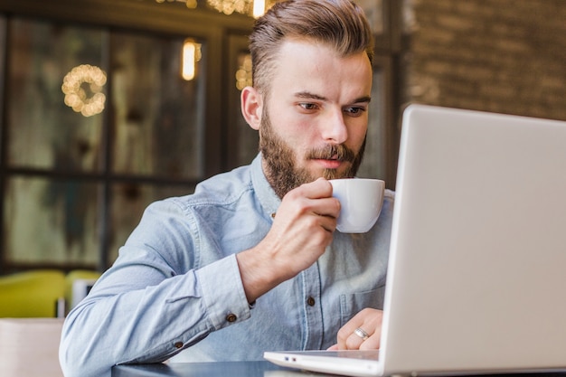 Hombre usando laptop tomando una taza de café