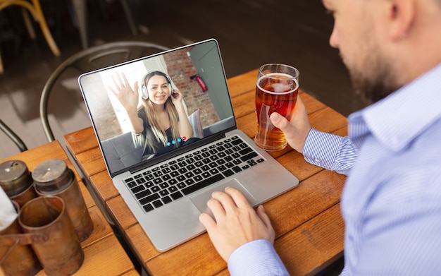 Hombre usando laptop para videollamada mientras bebe una cerveza