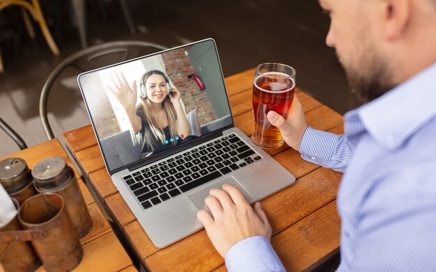 Hombre usando laptop para videollamada mientras bebe una cerveza