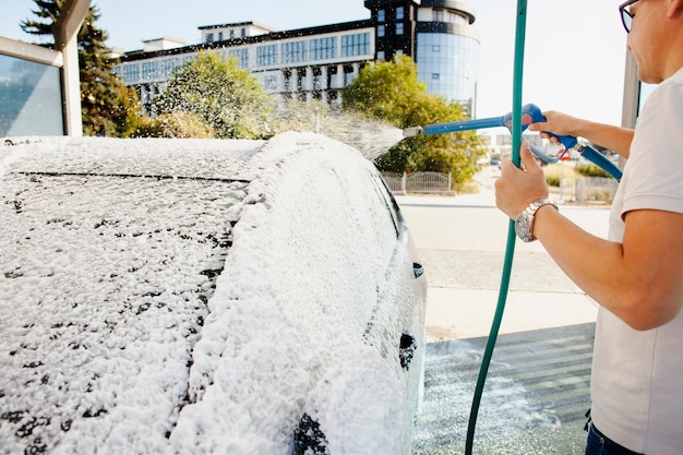 Foto gratuita hombre usando una manguera para limpiar su auto