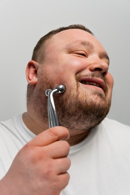 Foto gratuita hombre usando un rodillo de bolas en la cara para el cuidado de la piel