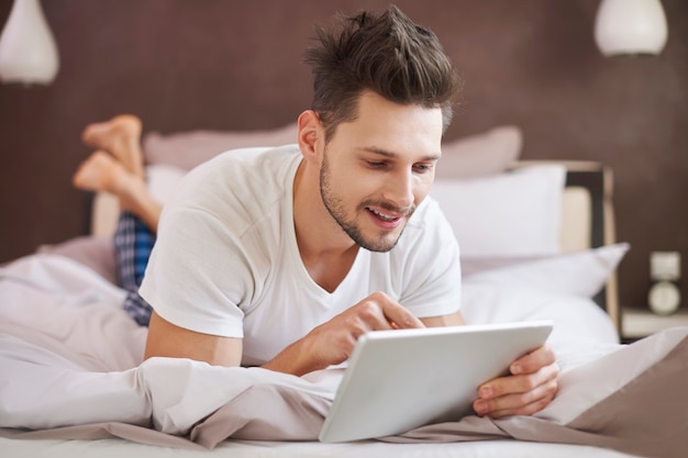 Hombre usando una tableta digital en el dormitorio