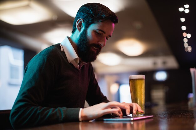 Hombre usando tableta digital con vaso de cerveza en mostrador