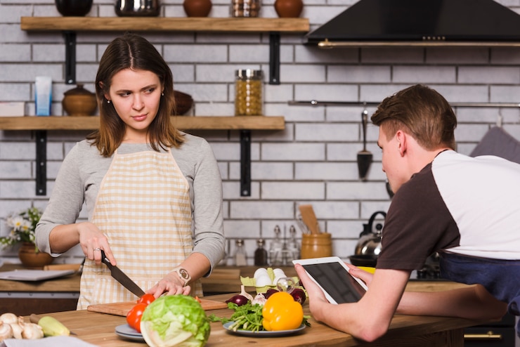 Foto gratuito hombre usando tableta mientras novia cortando verduras