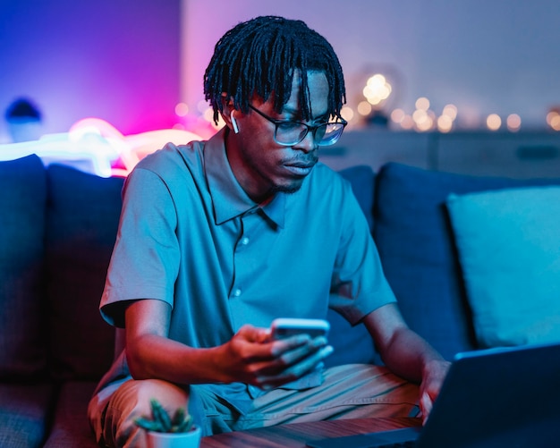 Hombre usando un teléfono inteligente y una computadora portátil mientras está en el sofá en casa