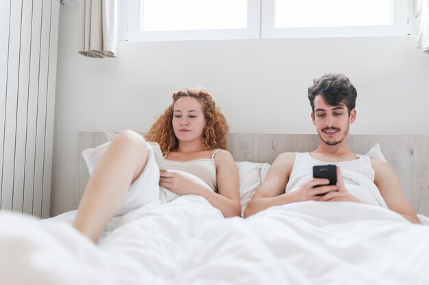 Hombre usando teléfono inteligente mientras que mujer leyendo un libro en el sofá