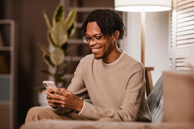 Hombre usando un teléfono inteligente moderno mientras está en el sofá en casa