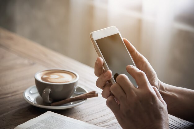 Hombre usando un teléfono móvil, tomando un café y leyendo un libro