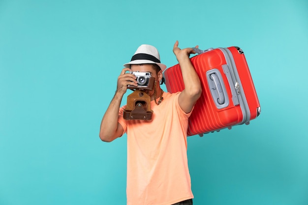 Hombre de vacaciones con maleta roja y cámara tomando fotos en azul