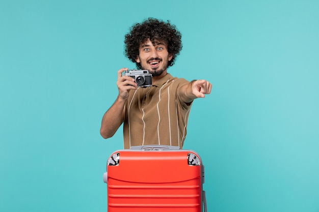Hombre de vacaciones con maleta roja tomando fotos con cámara en azul claro