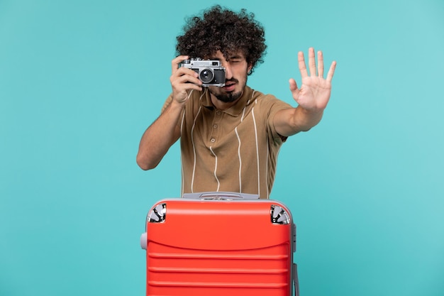 Hombre de vacaciones con maleta roja tomando fotos con cámara en azul