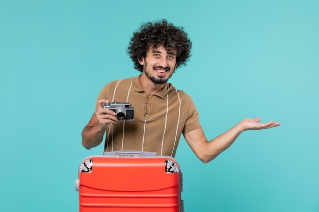 Hombre de vacaciones con maleta roja tomando fotos con cámara sonriendo sobre azul