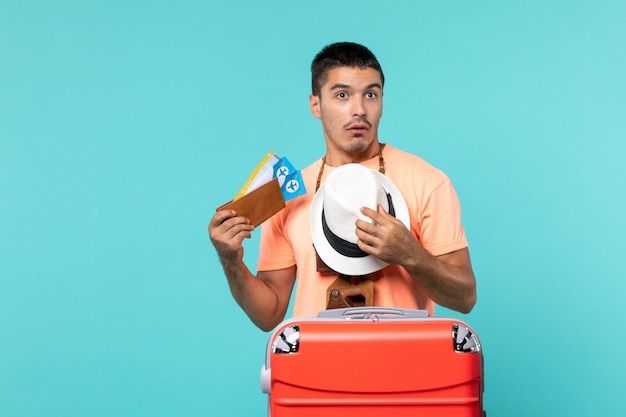 Foto gratuita hombre de vacaciones sosteniendo boletos con bolsa roja sobre piso azul viaje viaje de vacaciones viaje hidroavión