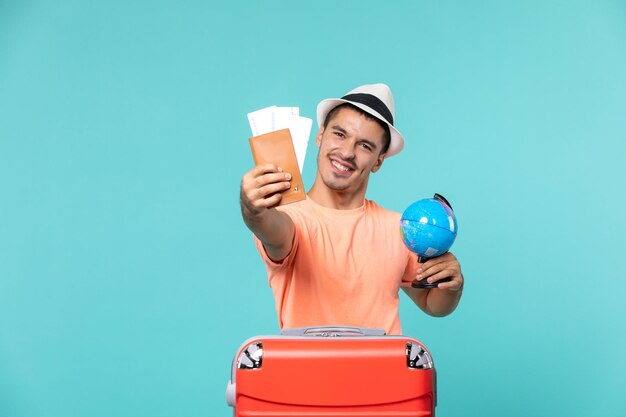 Hombre de vacaciones sosteniendo un globo terráqueo y entradas en azul claro