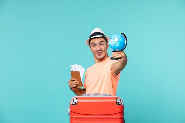 Hombre de vacaciones sosteniendo un globo terráqueo y entradas en azul claro