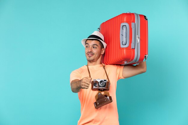 Hombre de vacaciones sosteniendo una gran maleta roja sobre azul claro