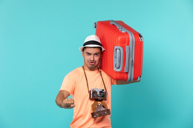 Hombre de vacaciones sosteniendo una gran maleta roja sobre azul