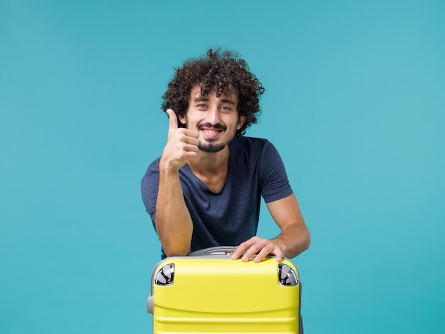 Foto gratuita hombre de vacaciones con su maleta amarilla sobre azul