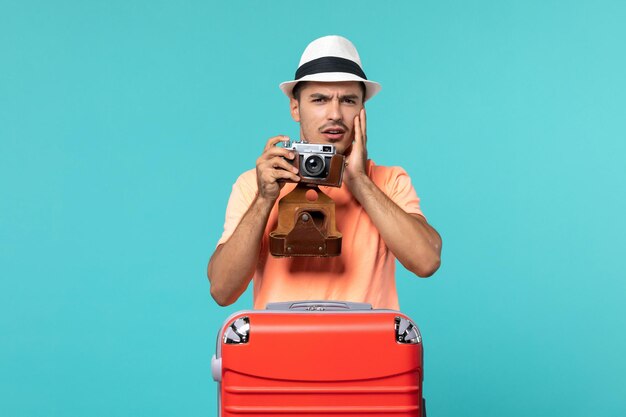 Hombre de vacaciones con su maleta roja tomando fotos con cámara en azul