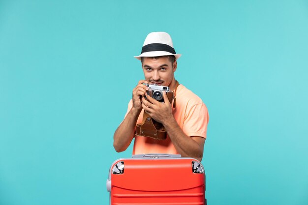 Hombre de vacaciones con su maleta roja tomando fotos con cámara en azul