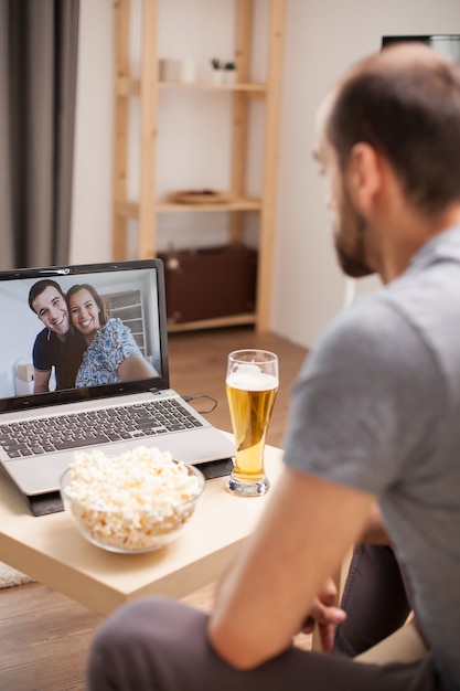 Hombre con un vaso de cerveza sobre la mesa en videollamada con sus amigos durante el distanciamiento social.