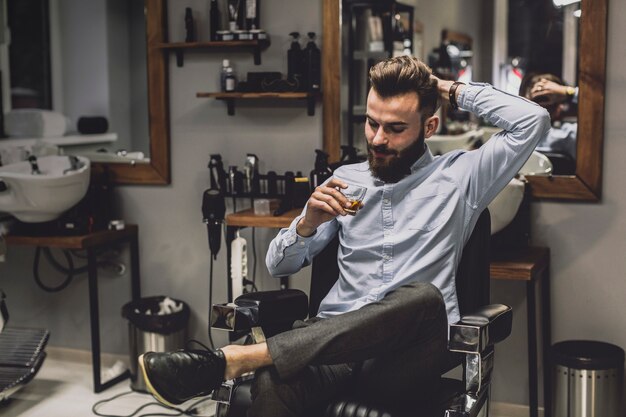 Hombre con vaso de licor en barbería