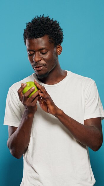 Hombre vegetariano jugando con manzana verde en estudio. Persona alegre tirando frutas, sintiéndose entusiasmado con una dieta y nutrición saludables. Adulto mirando a cámara y presentando bocadillos con vitaminas