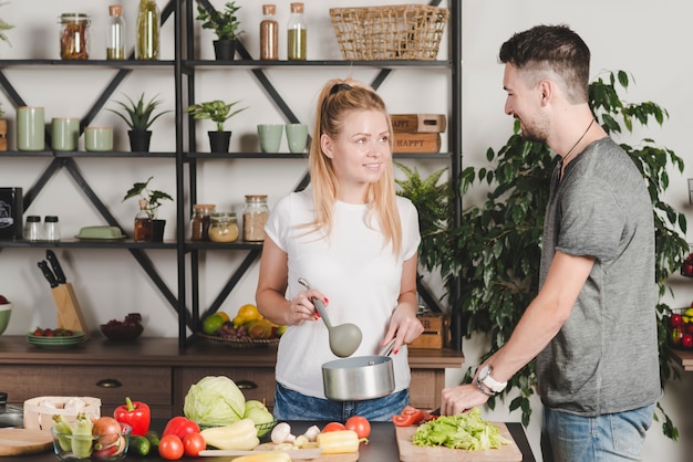 Hombre verduras de corte en la tajadera mirando a la mujer