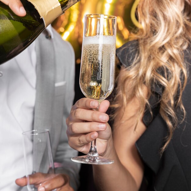 Hombre vertiendo champaña en vidrio sostenido por mujer close-up