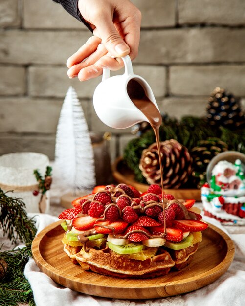 Hombre vertiendo chocolate sobre waffle con rodajas de fruta