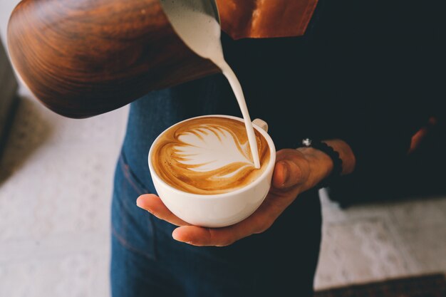 Hombre vertiendo leche en la decoración de espuma de café con leche