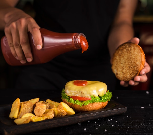 Foto gratuita hombre vertiendo salsa de tomate en sabrosa hamburguesa de ternera