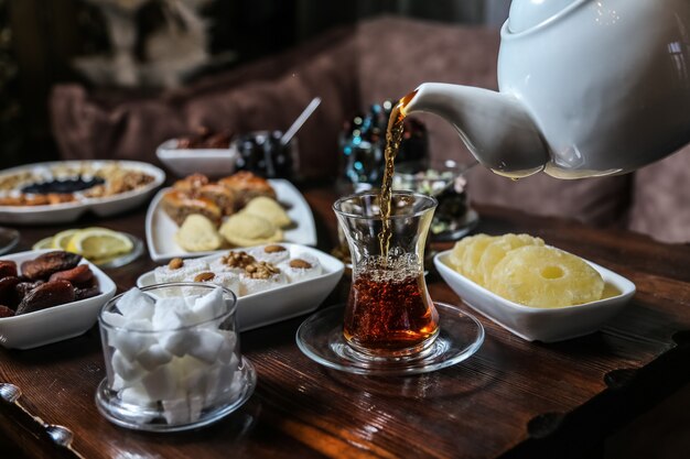 Hombre vertiendo té en armudy juego de té de frutas secas de azúcar vista lateral