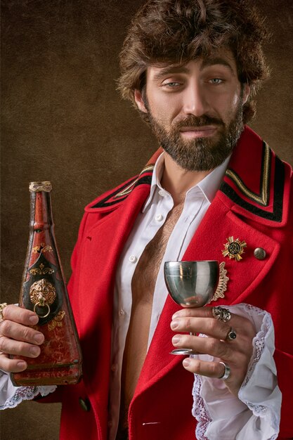 Hombre vestido con abrigo rojo y negro de pie y sosteniendo la botella y copa de vino