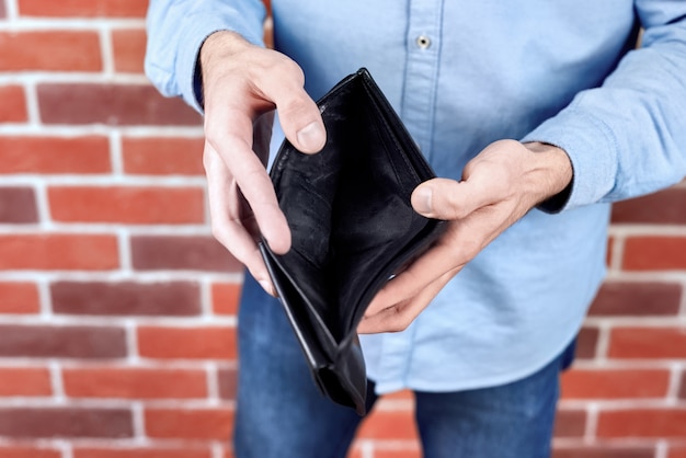 Hombre vestido con camisa azul que muestra una billetera negra vacía