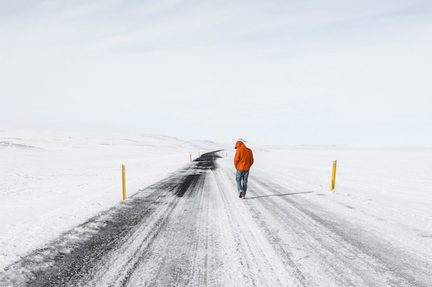 hombre vestido con chaqueta naranja caminando por una carretera nevada