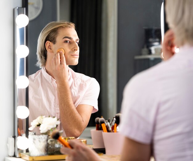 Hombre vestido con maquillaje con base y mirando en el espejo