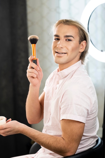 Foto gratuita hombre vestido con maquillaje y sosteniendo una vista lateral del cepillo