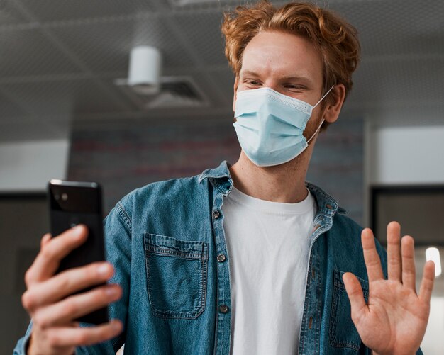 Hombre vestido con máscara médica y mirando el teléfono