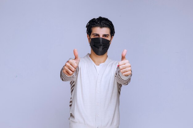 Hombre vestido con una máscara negra y haciendo pulgar hacia arriba.