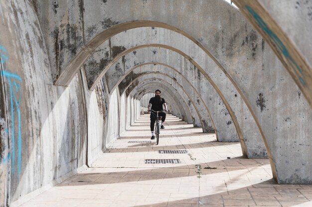 Un hombre vestido de negro andando en bicicleta en el arco.