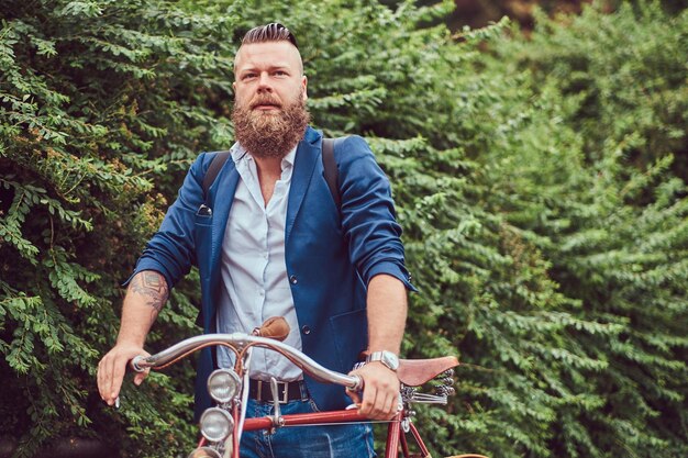 Hombre vestido con ropa informal, de pie con una bicicleta retro en un parque de la ciudad.