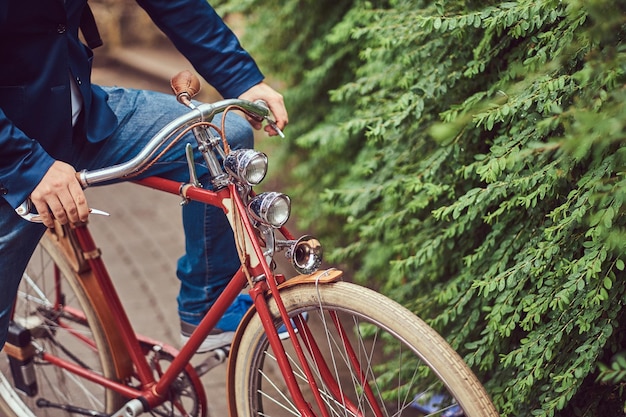 Hombre vestido con ropa informal, sentado en una bicicleta retro en un parque de la ciudad.