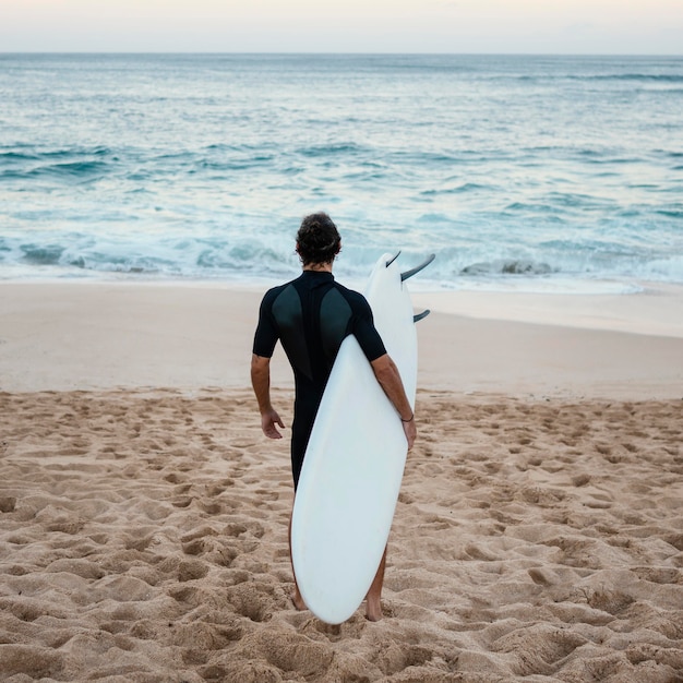 Hombre vestido con ropa de surfista caminando sobre la arena desde atrás