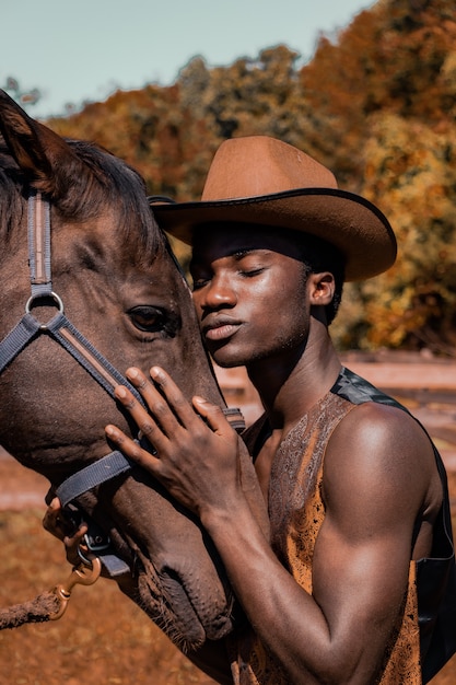 Hombre vestido con sombrero de vaquero marrón y abrazando a caballo