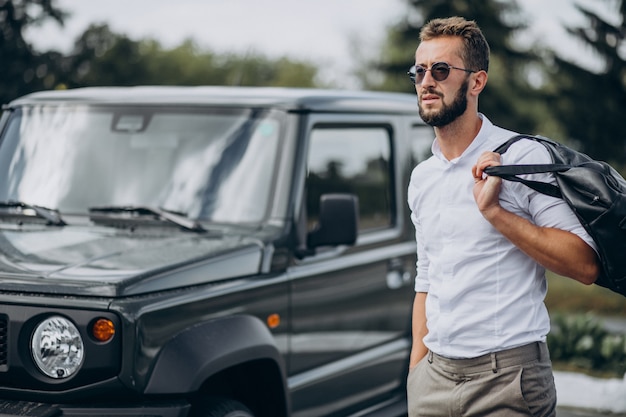 Hombre viajando con bolsa y de pie junto al coche.