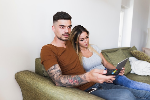 Hombre viendo la televisión con su novia usando la computadora portátil en casa