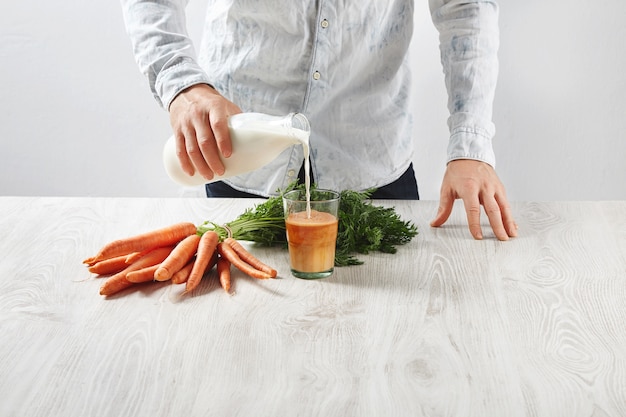 El hombre vierte la leche de la botella al vaso con jugo de zanahoria natural recién exprimido