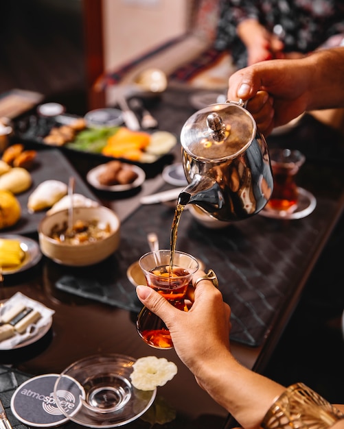 El hombre vierte el té de la tetera en un vaso armudu servido para preparar el té